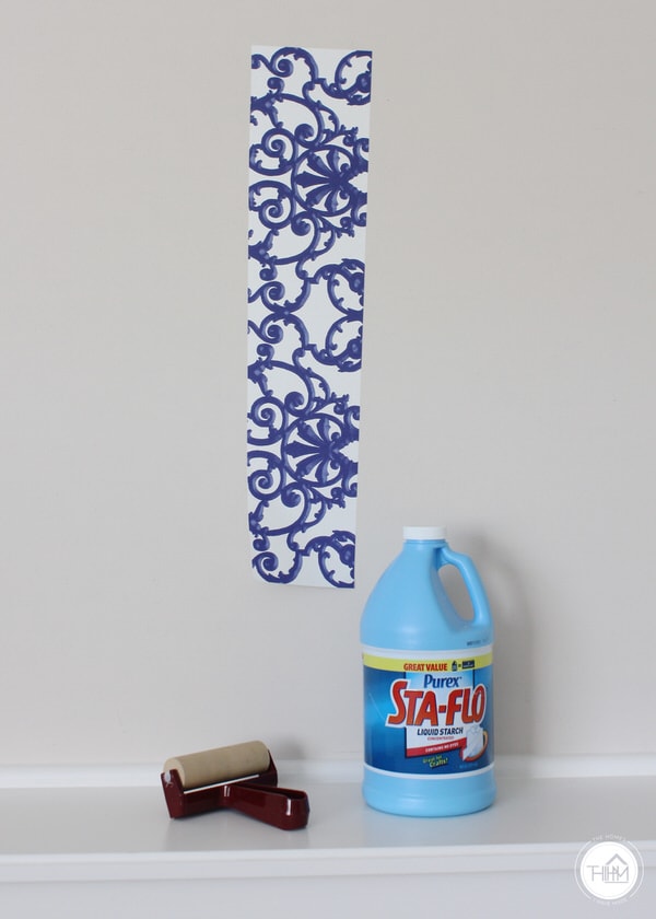 Liquid starch, a roller, and a strip of wallpaper secured to a wall