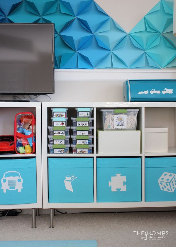 Photo of cubby shelves containing toys, cloth bins and clear bins containing Legos organized below a TV 