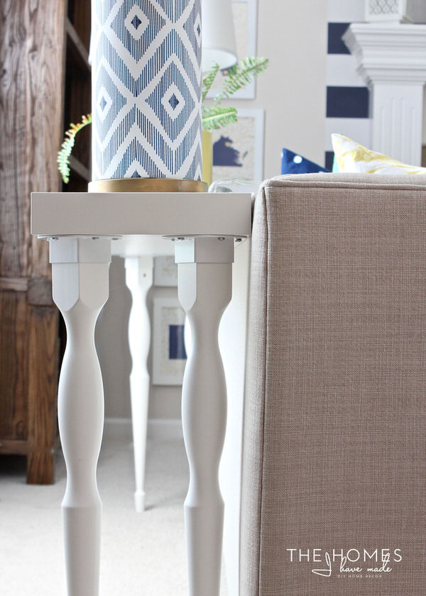 Vertical image of a sofa table with a lamp placed on top behind a beige couch