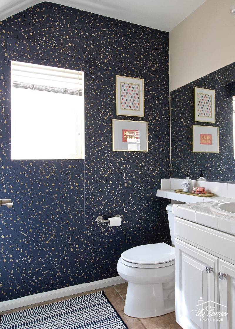A rental bathroom decorated with gold splatter wallpaper, gold and salmon bathroom accents, and a navy and white rug