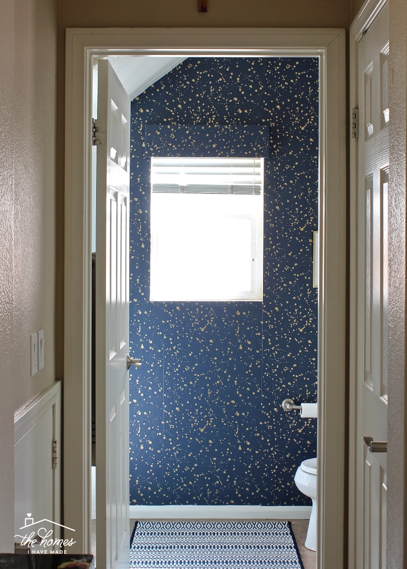 A rental bathroom decorated with gold splatter wallpaper and a navy and white rug