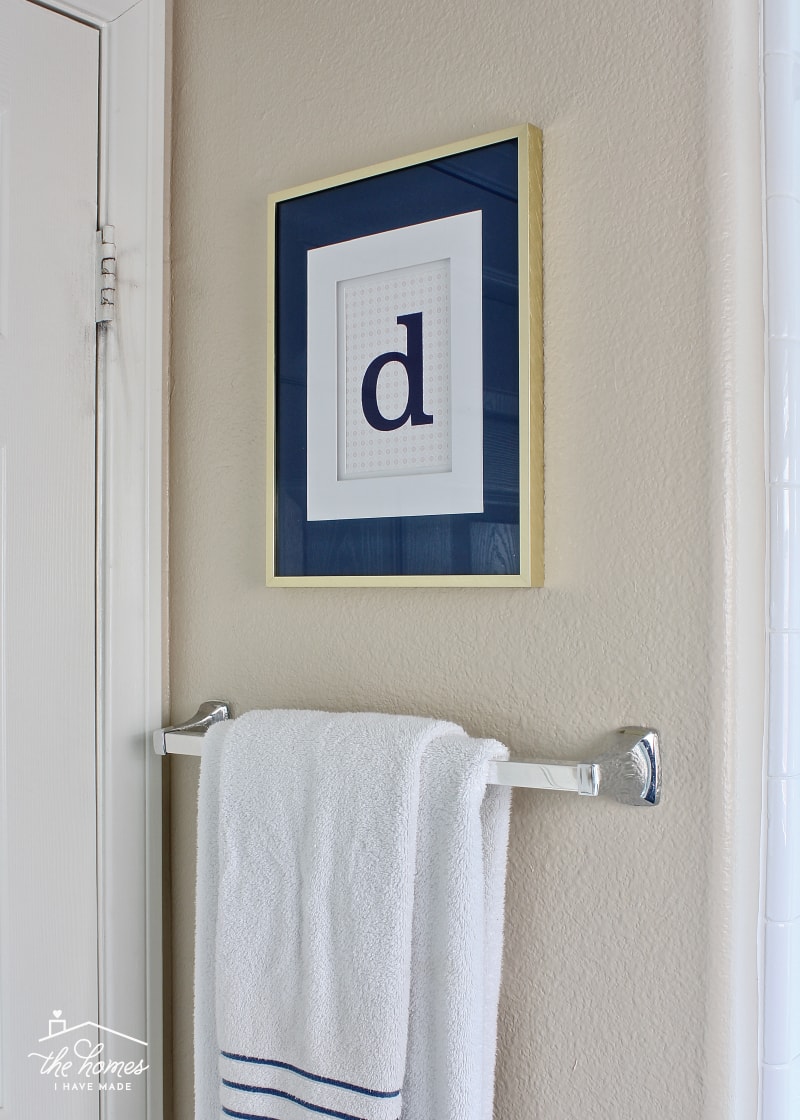 A gold-framed monogrammed letter and a towel bar with a white towel hanging