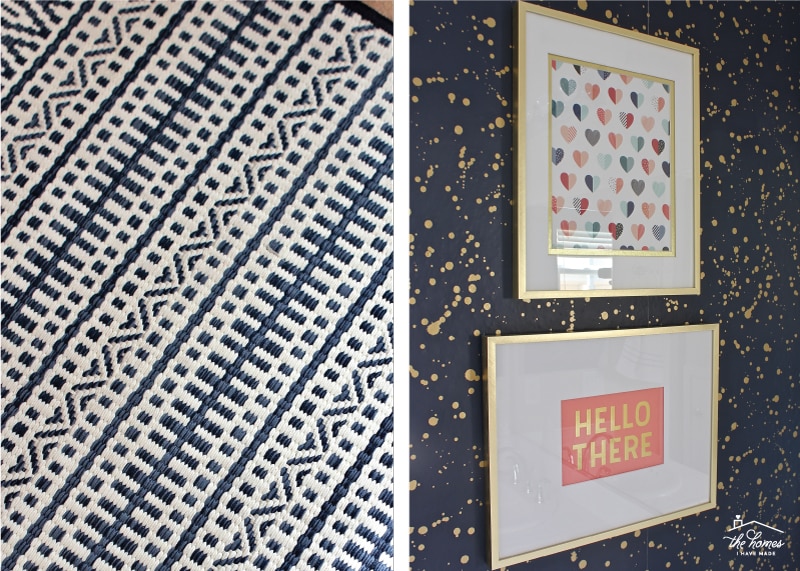 A textured bathroom rug in navy and white geometric patterns and a wallpapered bathroom wall with artwork in gold frames