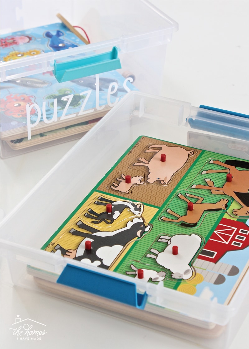 Vertical image of two clear boxes containing wooden kid puzzles and labeled on the outside with the word "puzzles"
