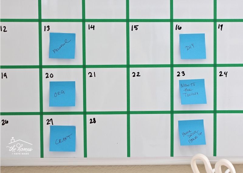 A dry-erase board calendar with grid lines made from washi tape and post-it notes on various days