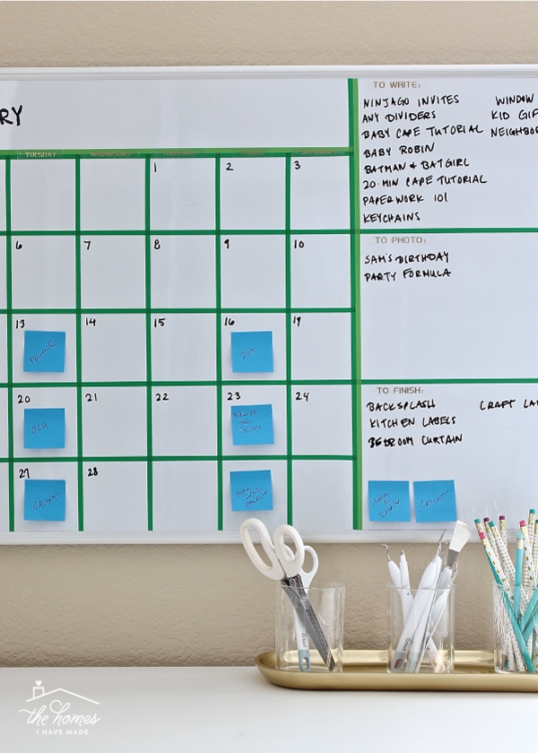 A dry-erase board calendar with grid lines made from washi tape with words and post-it notes