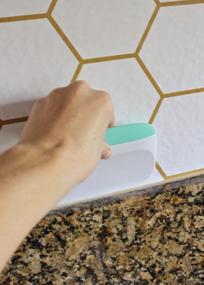 Hand smoothing down peel and stick wallpaper with a scraper over a backsplash