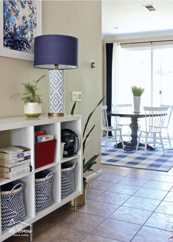 A foyer with a shelving unit and decor and a rug under a kitchen table and chairs