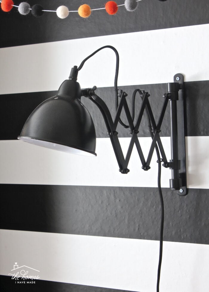 Black accordion sconce hung on black-and-white striped wallpaper