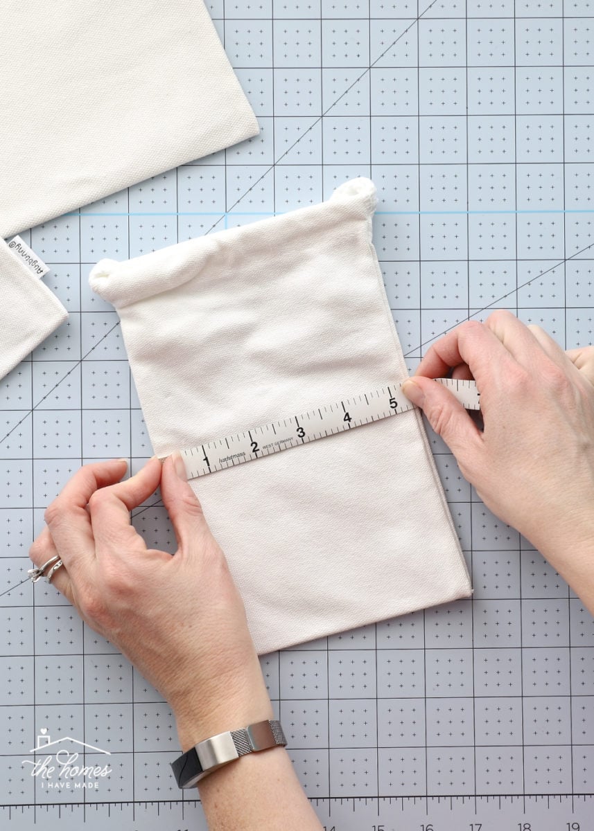 Hands measuring a small canvas bag with a measuring tape