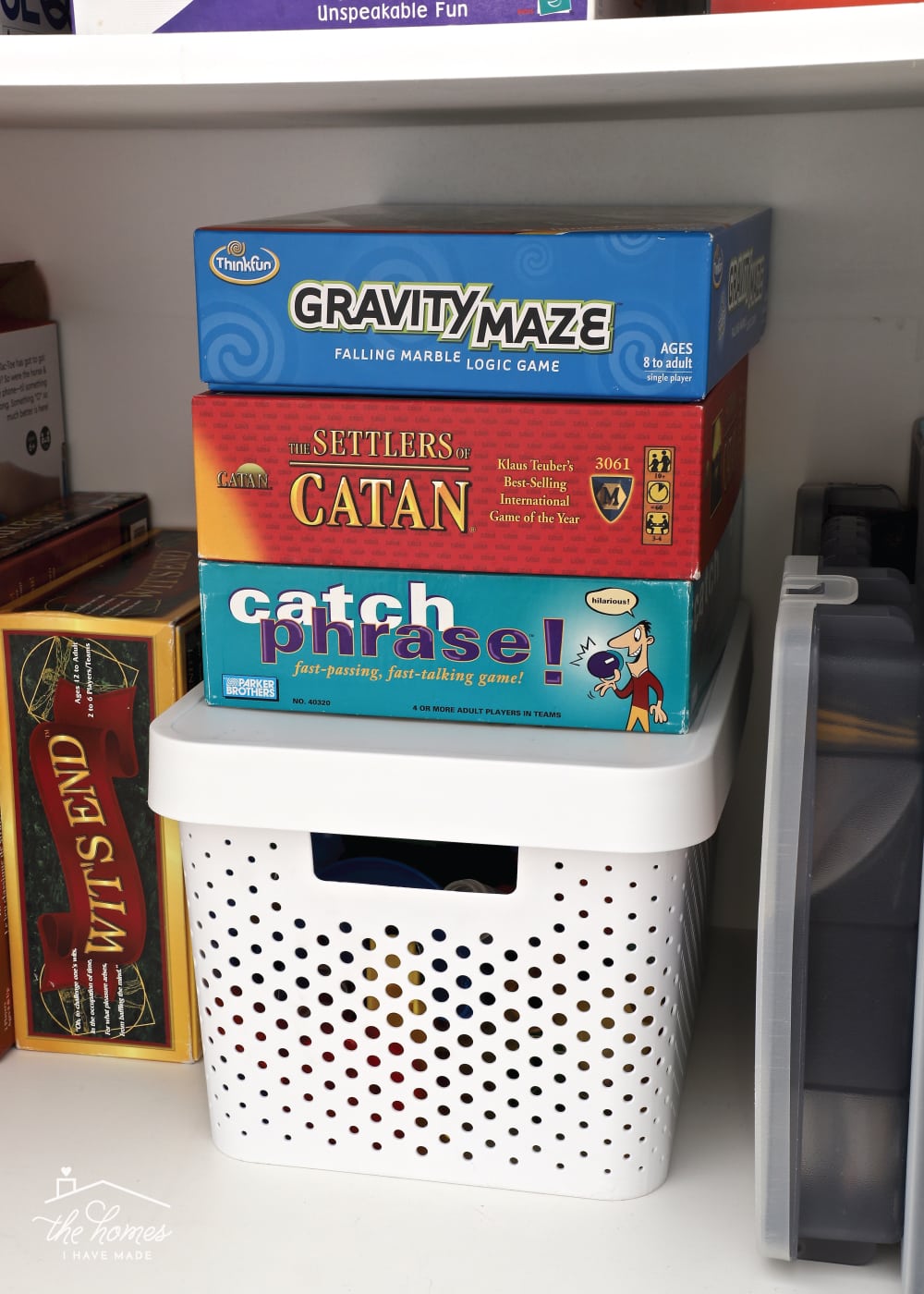 Vertical image of a variety of board games stacked vertically on top of a white storage basket inside a cabinet