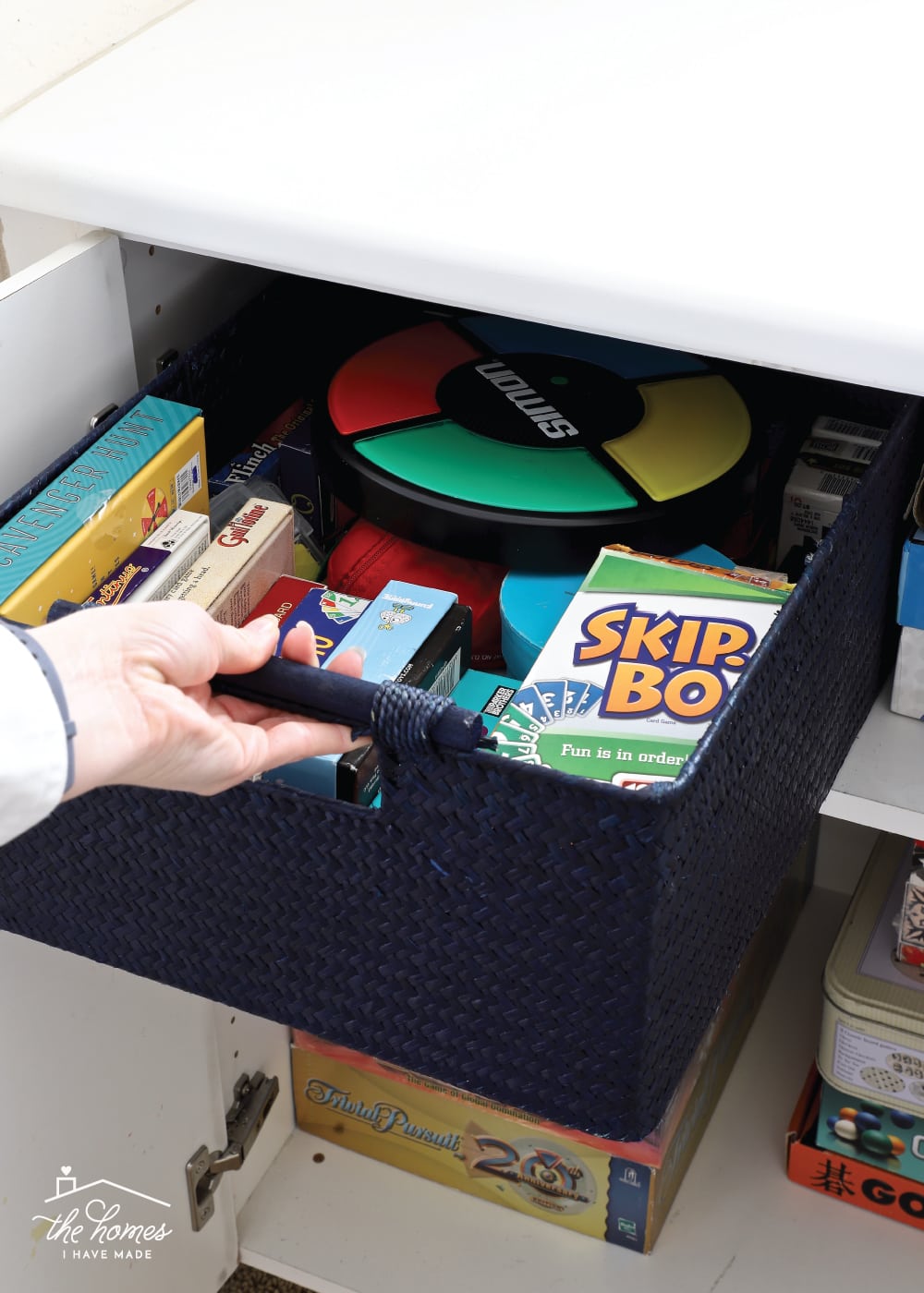 Vertical image of a hand pulling the handle of a basket containing card games out of a cabinet