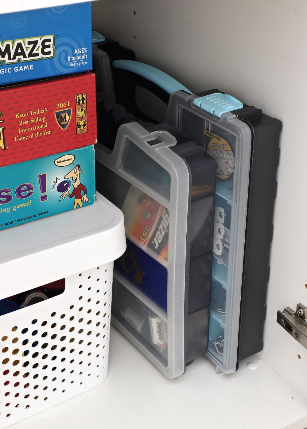 Vertical image of game boards stacked vertically on top of a storage bin to the left of plastic organizing totes