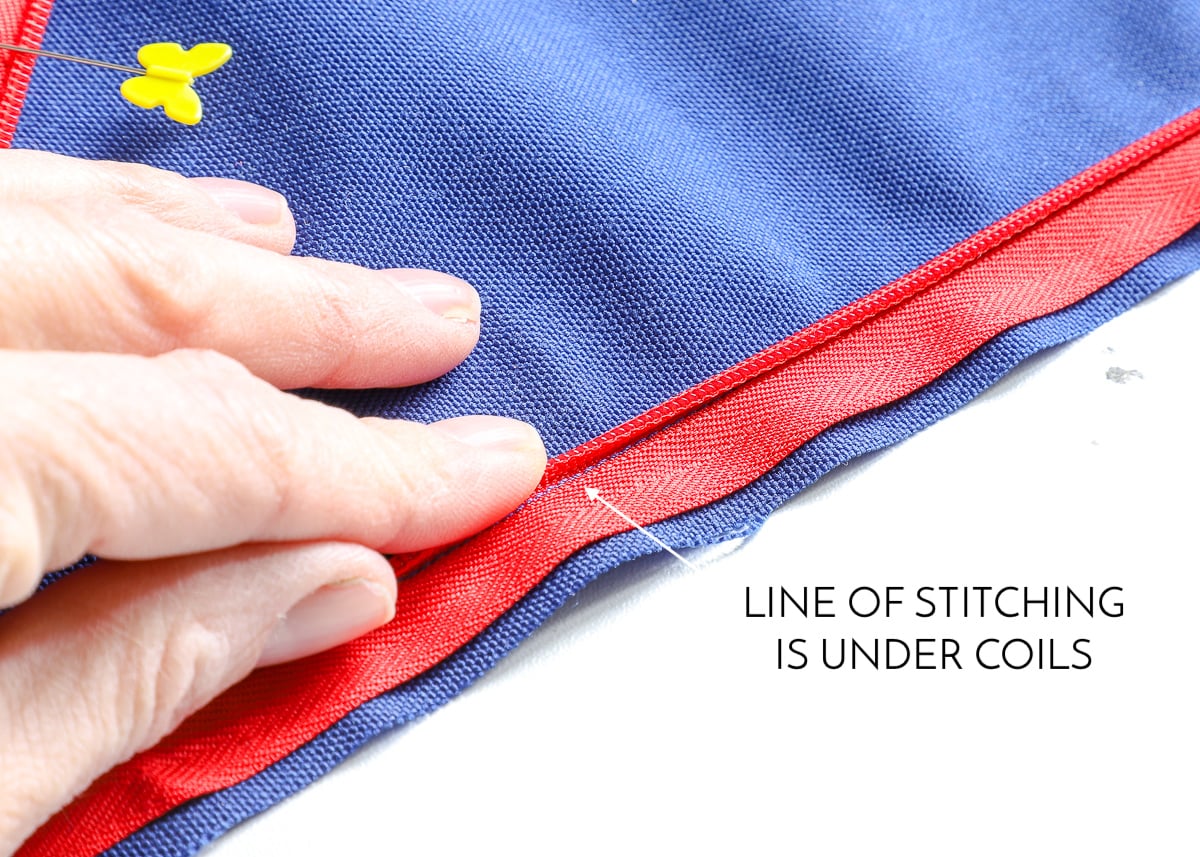 A hand placed on blue fabric with red invisible zipper revealing a line of stitching under coils 