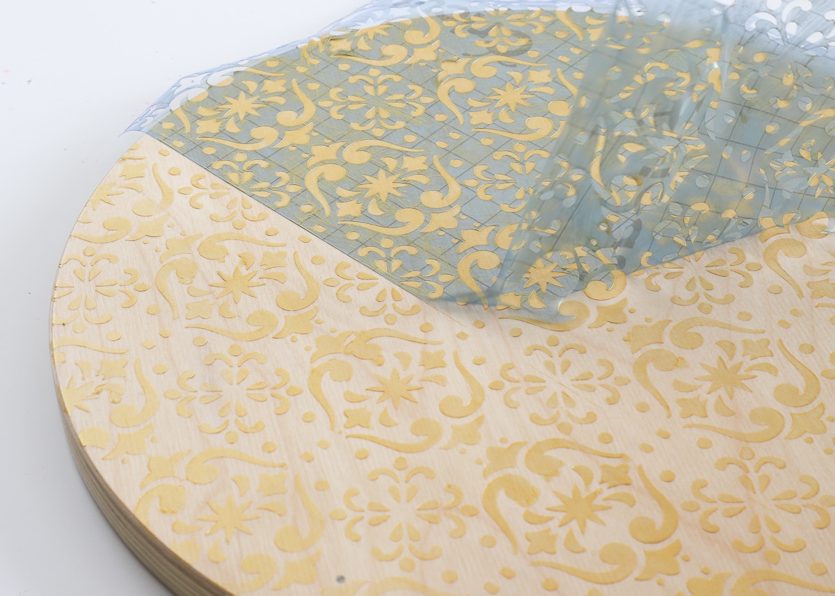 Removing stencil vinyl from a wooden stool painted with gold paint