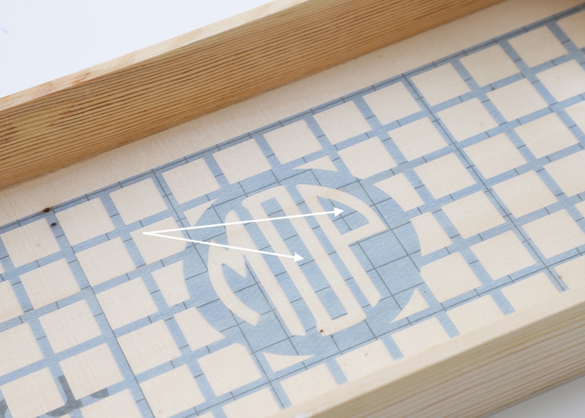 Stencil vinyl placed into a wooden tray with arrows showing gridlines