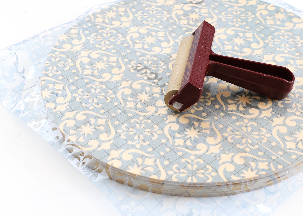 A light blue vinyl stencil on a wooden stool shown with craft brayer