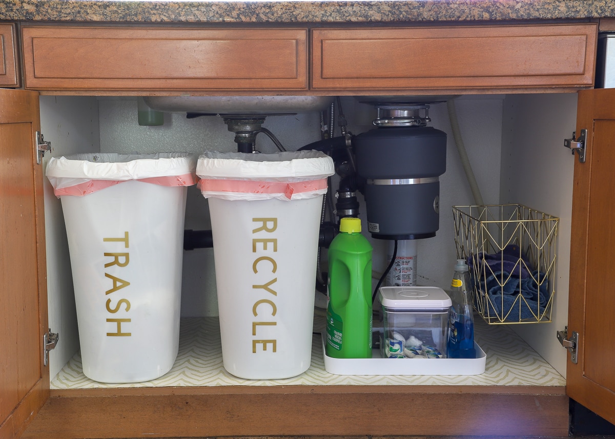Dirty dish towels, dish washing supplies, and trash cans organized in a cabinet under the sink