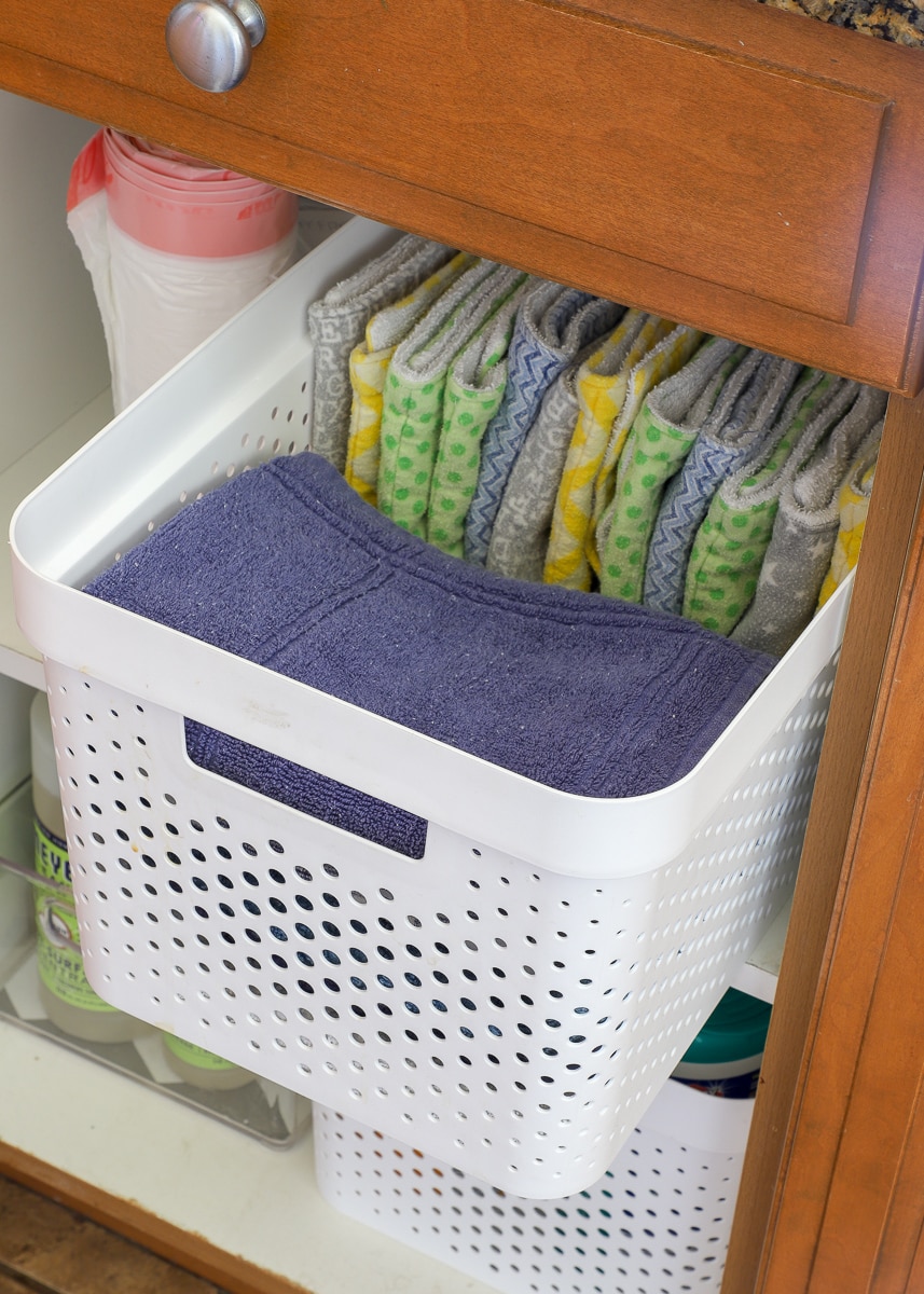 Clean, folded dish towels in an open bin placed in lower kitchen cabinet