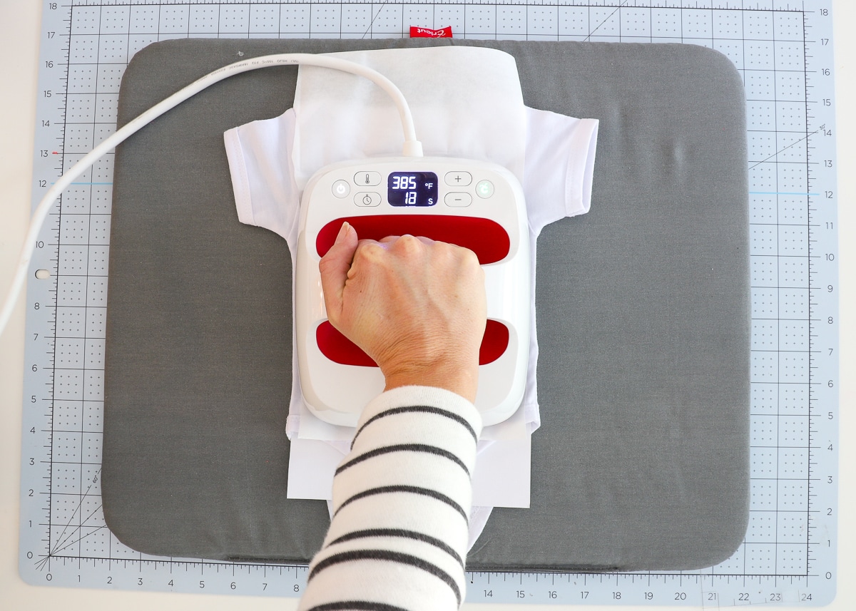 Hand pressing an EasyPress 2 onto a baby onesie