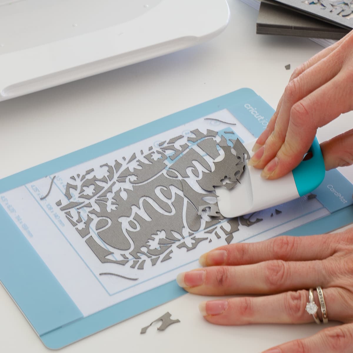 A scraper tool removes negative card space from a Cricut card mat