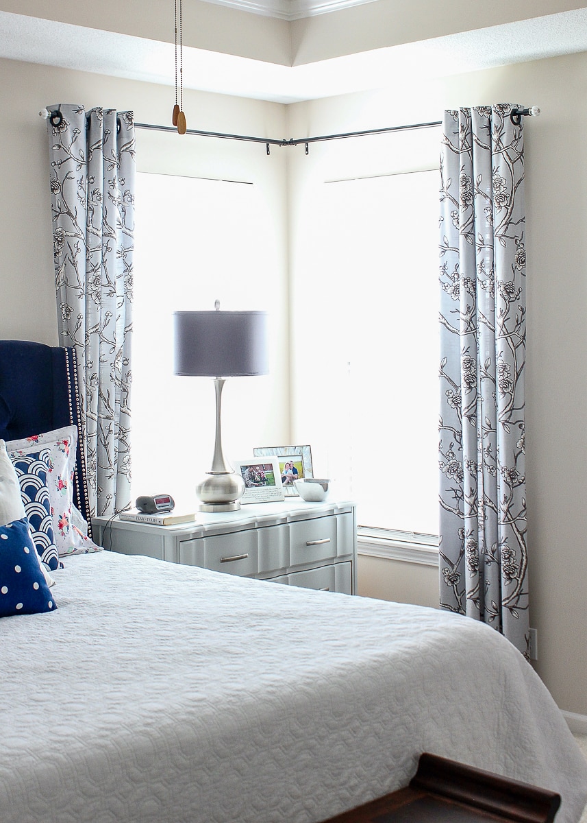 A corner window with curtains in a master bedroom