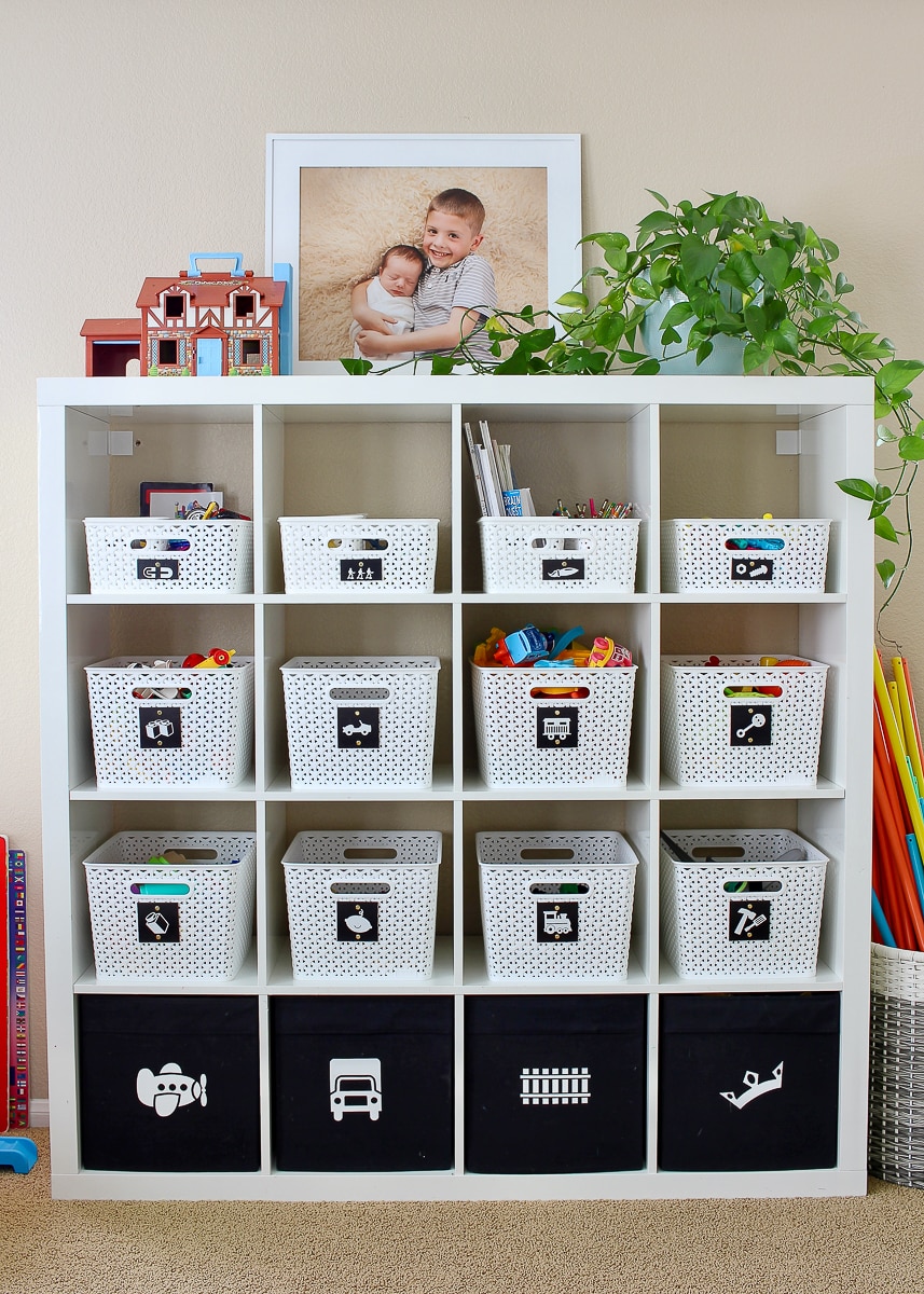 White baskets with black labels filled with toys on an IKEA Kallax shelf
