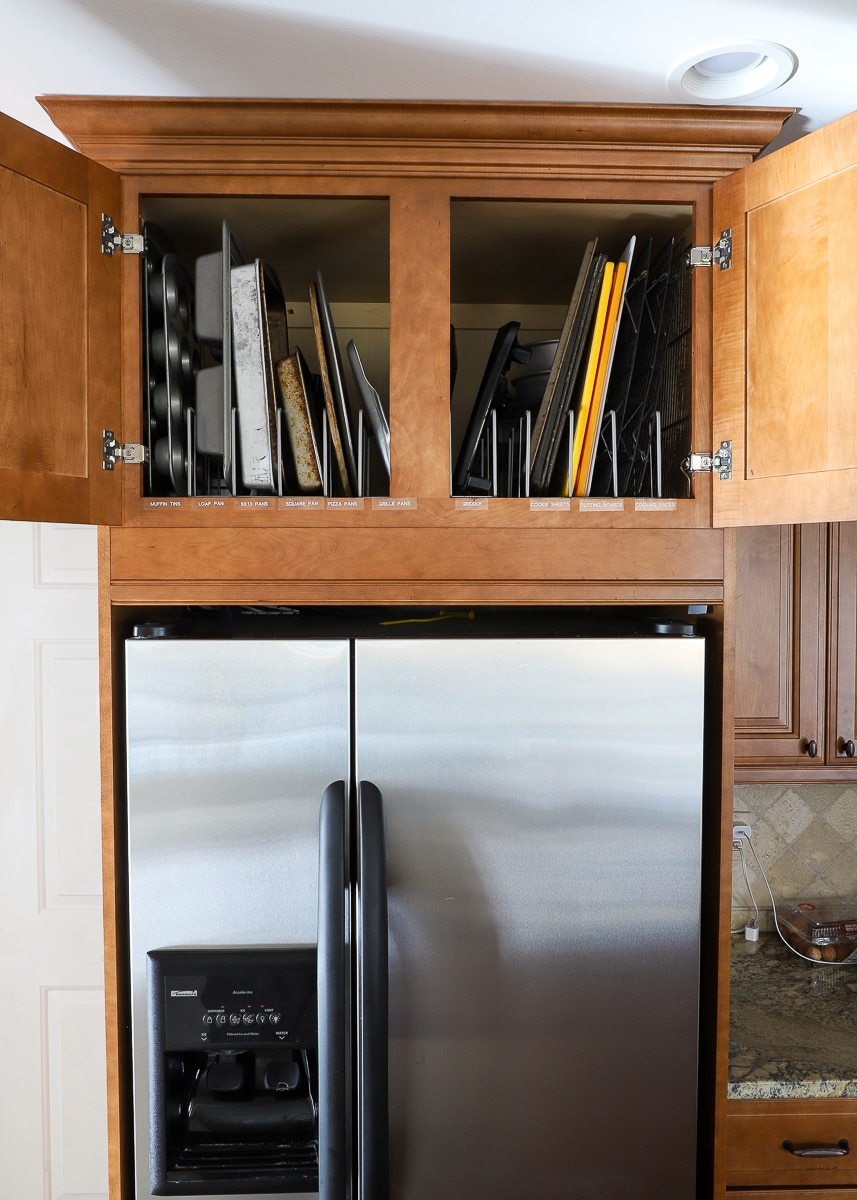 Cookware organized and labeled inside a cabinet above a refrigerator 