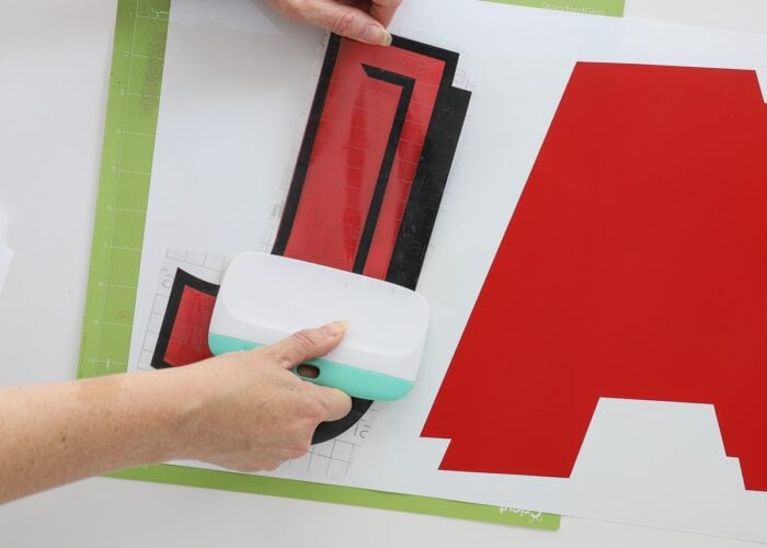 Hands using transfer tape to layer red and black vinyl letters