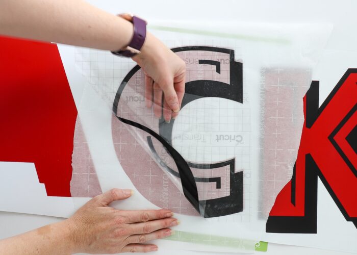 Hands using transfer tape and parchment paper to layer red and black vinyl letters