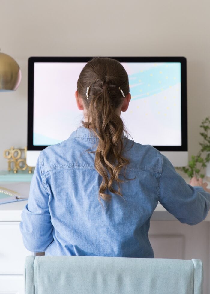 Rear shot of a girl in a blue shirt facing a computer.