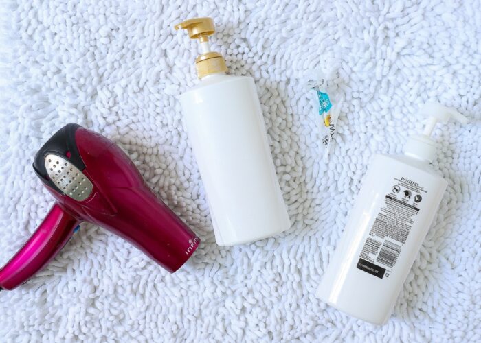 White shampoo and conditioner bottles on a white carpet shown with a hair dryer.