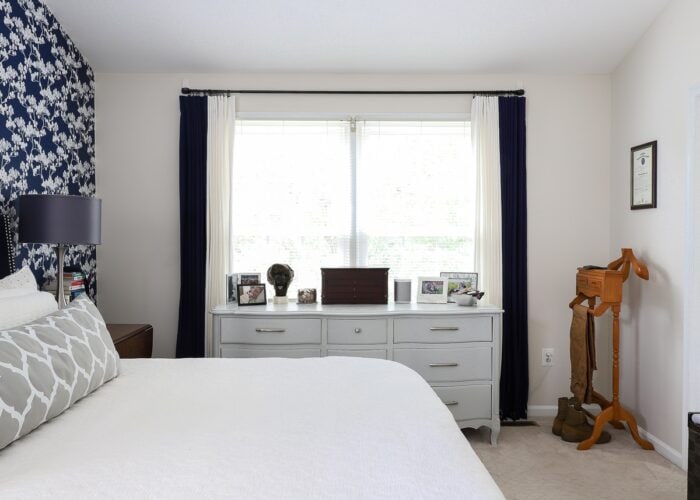 A rental bedroom with a long grey dresser and white and navy curtains.