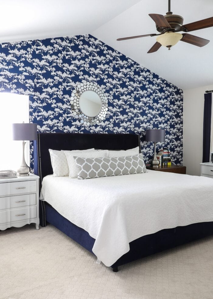 Rental bedroom with blue and white flowered wallpaper, a navy bed, and grey lamps.