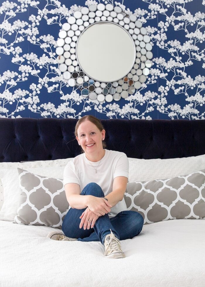 Megan Duesterhaus sitting on a navy bed with a grey pillow and white bedspread.