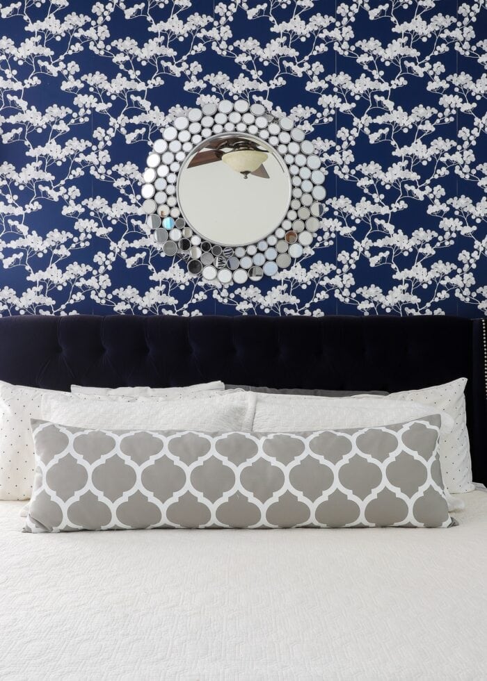 Rental bedroom with blue and white flowered wallpaper, a navy bed with a white bedspread, and a silver mirror above the bed.
