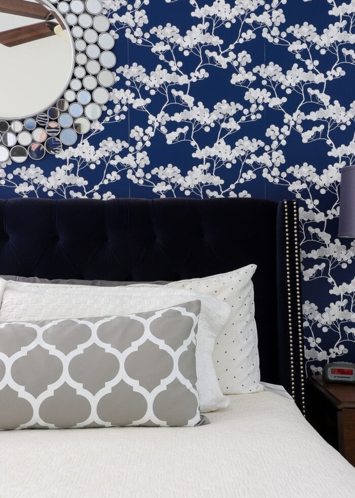 Rental bedroom with blue and white flowered wallpaper and a navy velvet bed with white and grey pillows.