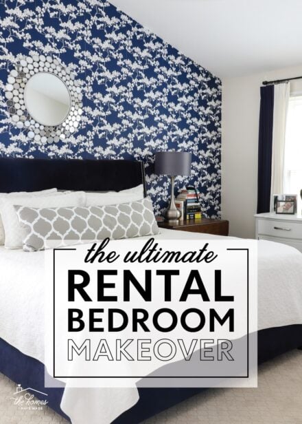 Rental bedroom with blue and white flowered wallpaper, a navy bed, and grey lamps.