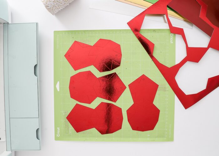 Red Foil Kraft Board on Green Cricut mat cut into paper star ornaments