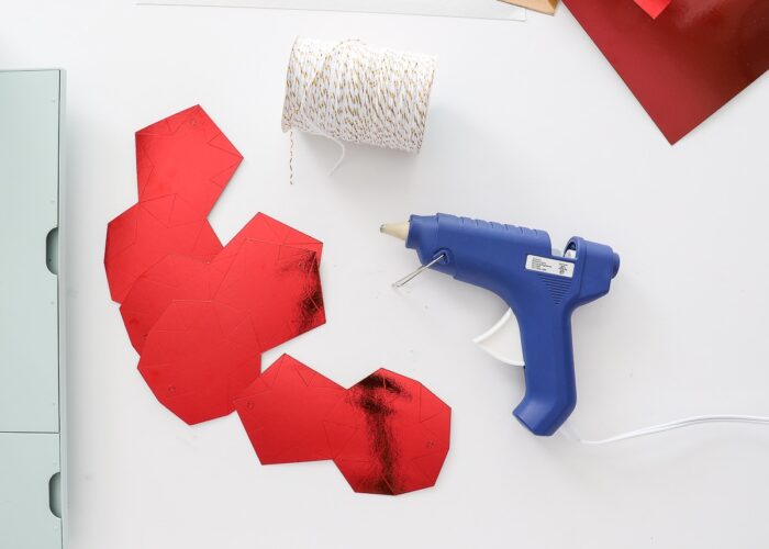 Red Foil Kraft Board cut into paper star ornaments shown with hot glue gun.