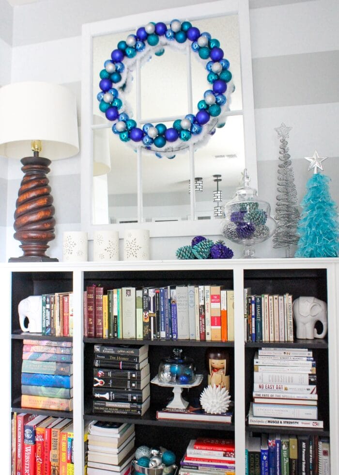 Blue, white and turquoise Christmas ornaments wreath above bookcase.