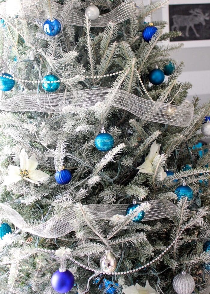 White flocked tree with blue, silver, and turquoise Christmas ornaments.
