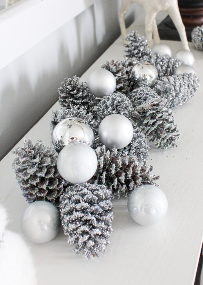 Silver glittered pinecones on a mantel display.