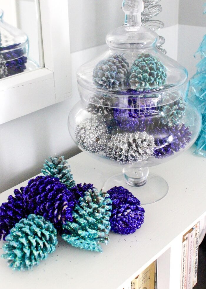 Navy and turquoise glittered pinecones in glass jar.