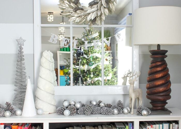 Silver glittered pinecones on a mantel display with white and silver trees.