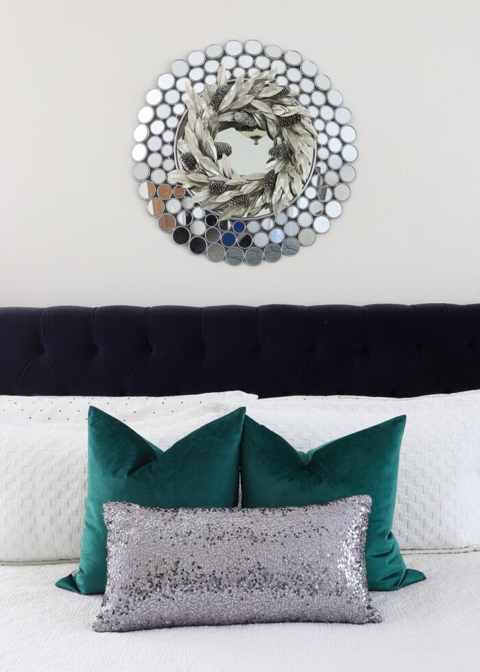 Green velvet pillows on a bed with a silver mirror above.