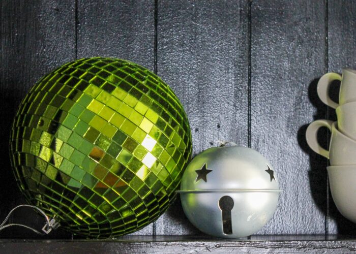 Large green Christmas ornament next to silver bell.