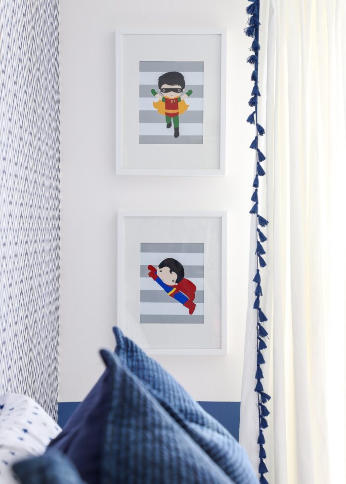 White frames with super hero prints on a white wall with blue pillows
