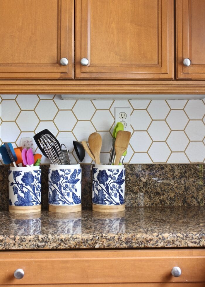 Blue and white flowered utensil jars on a granite countertop against a wallpapered backsplash on rental walls