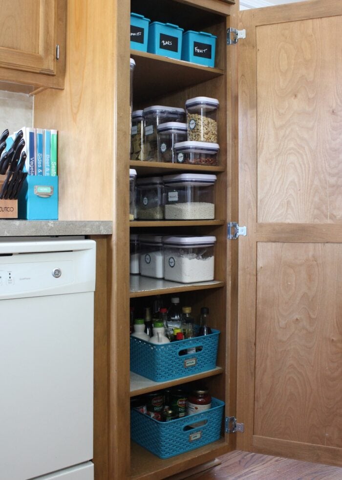A skinny pantry organized with blue baskets and white containers